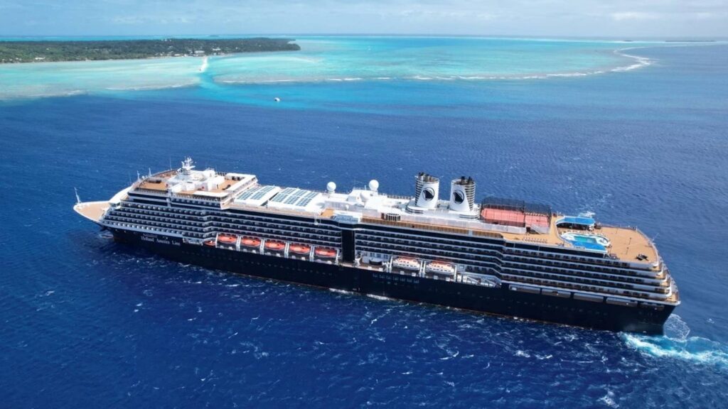 Large cruise ship sailing in blue ocean near a tropical island with clear skies and turquoise waters in the background.