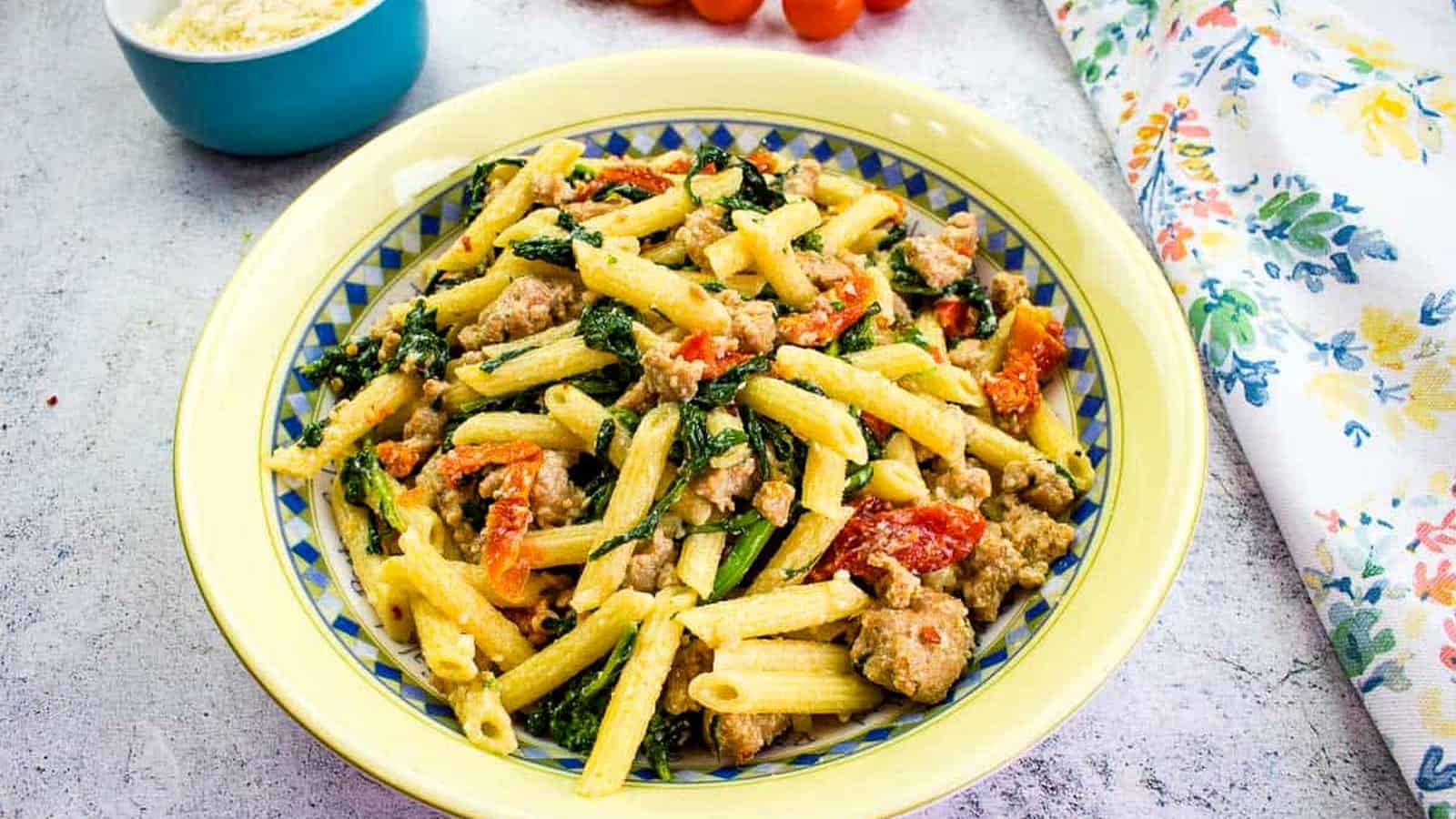 Broccoli Rabe and Sausage in a serving bowl with tomatoes in the background.