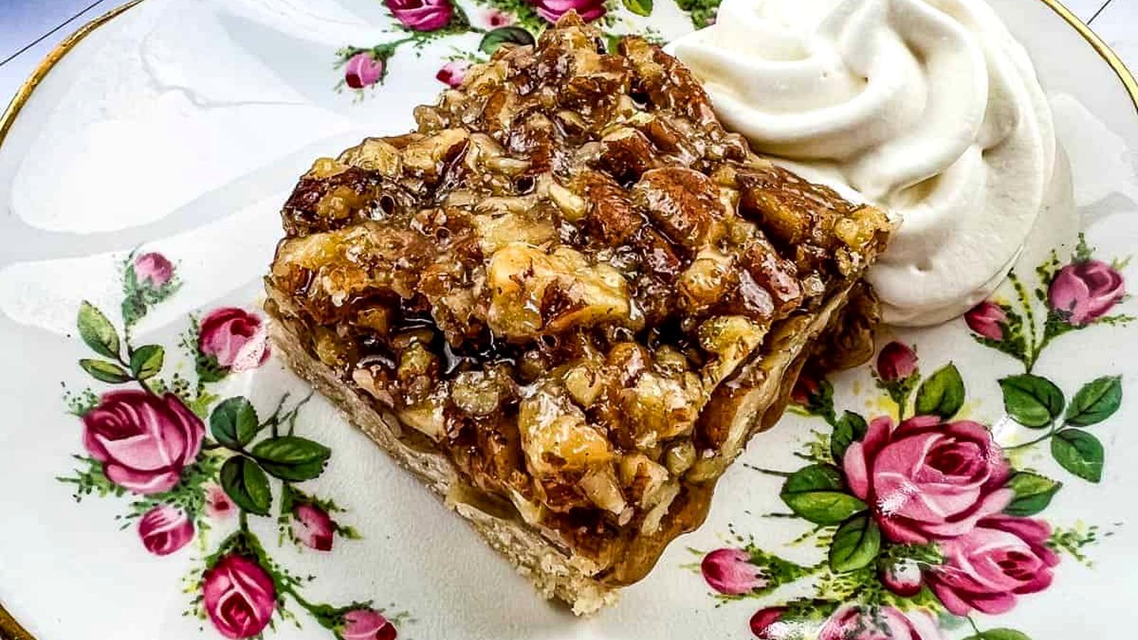 A slice of maple pecan pie bar topped with chopped pecans sits on a floral-patterned plate.