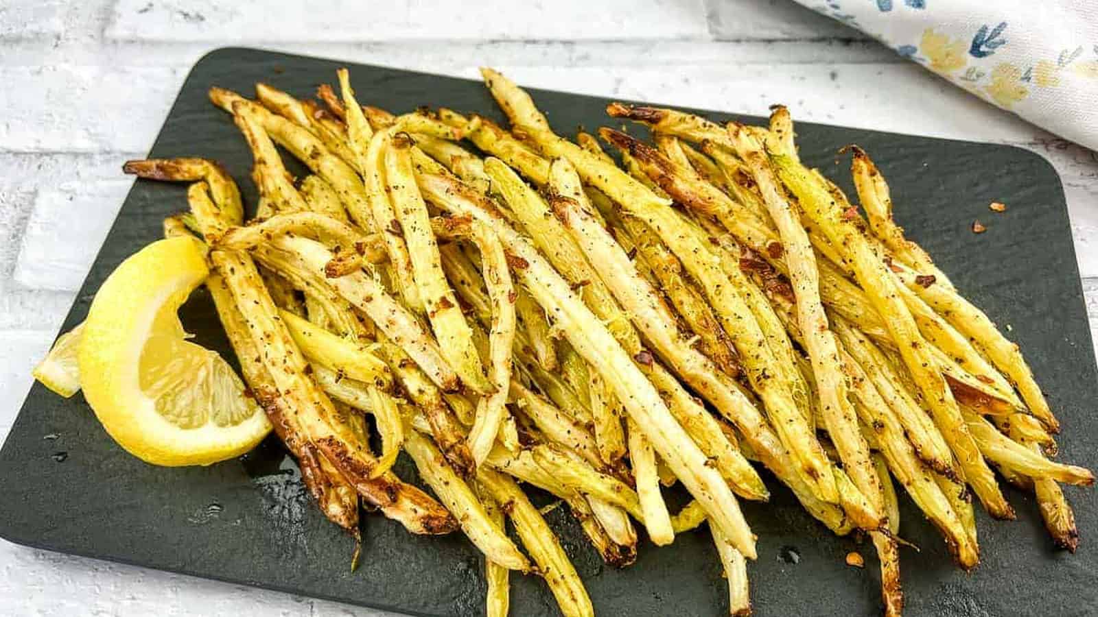 Lemon pepper yellow beans on a black plate with lemon wedges.