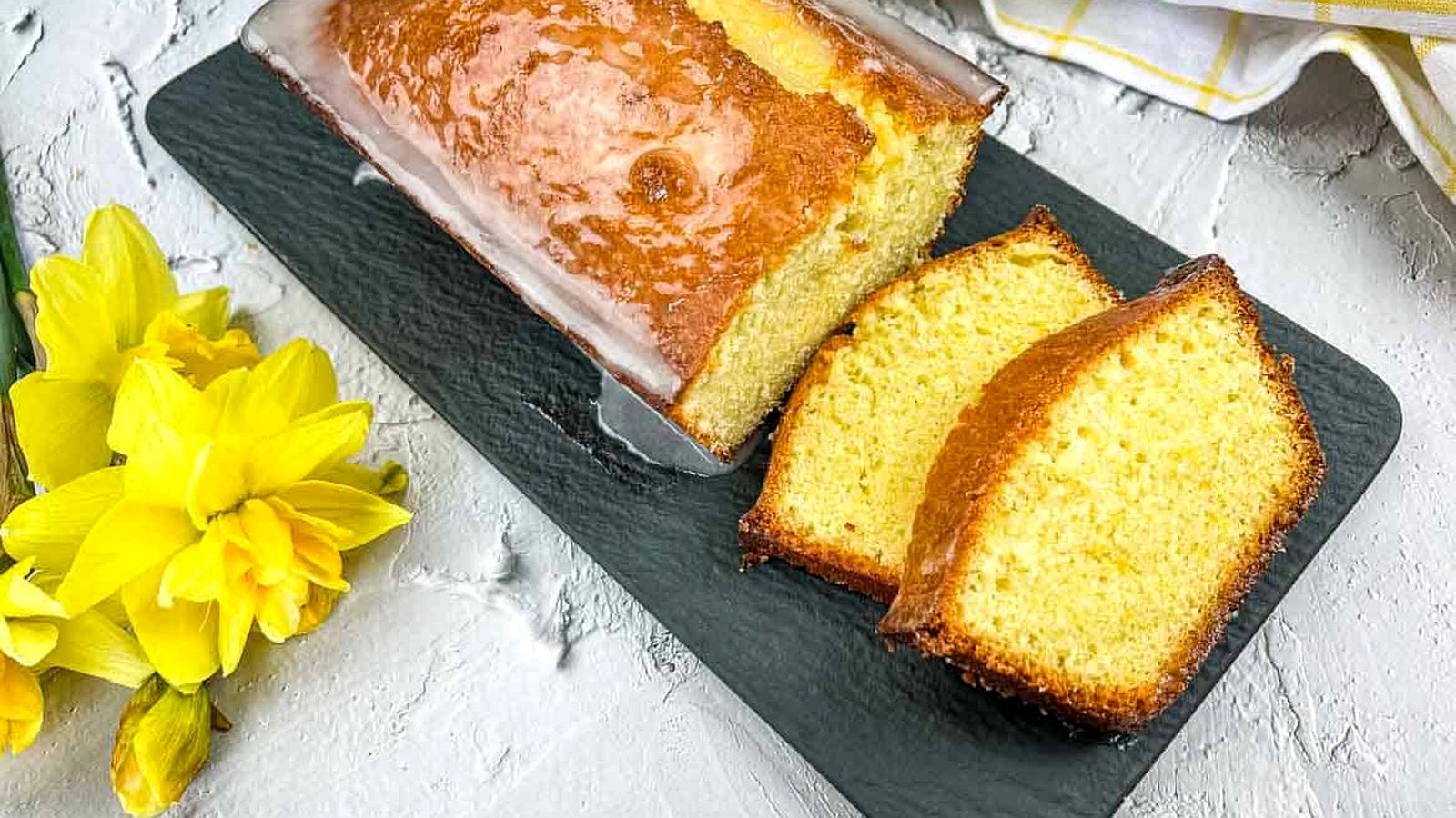A slice of lemon pound loaf on a plate with daffodils.
