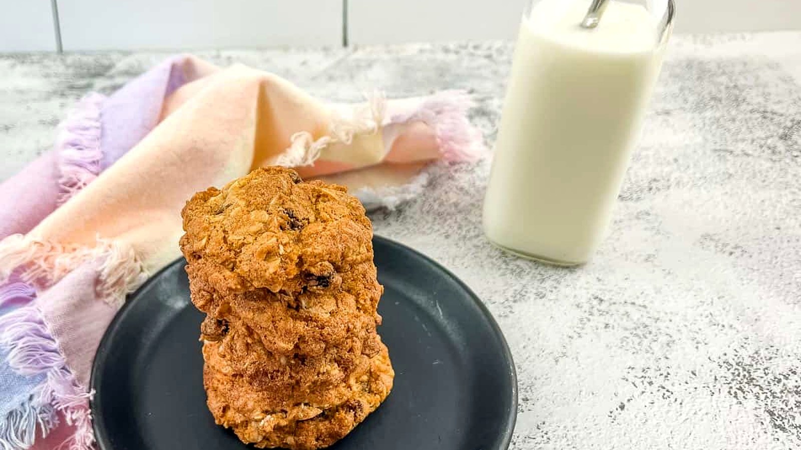 Oatmeal raisin cookies on a plate next to a glass of milk.