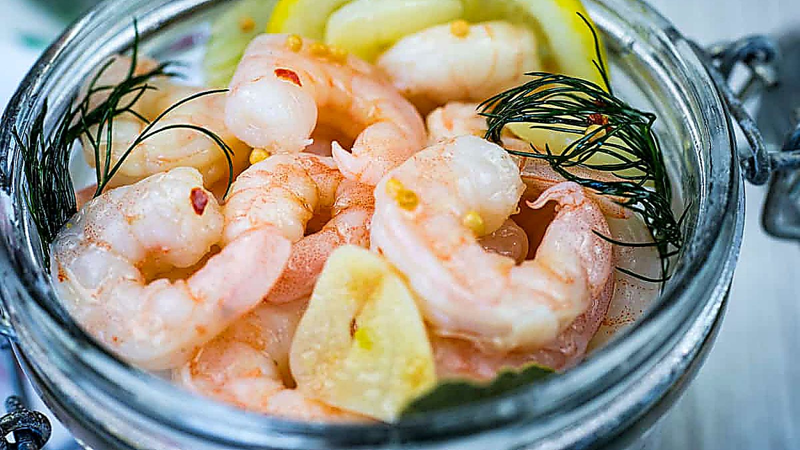 Open jar filled with Southern Style Pickled Shrimp, dill, lemon slices, and herbs.