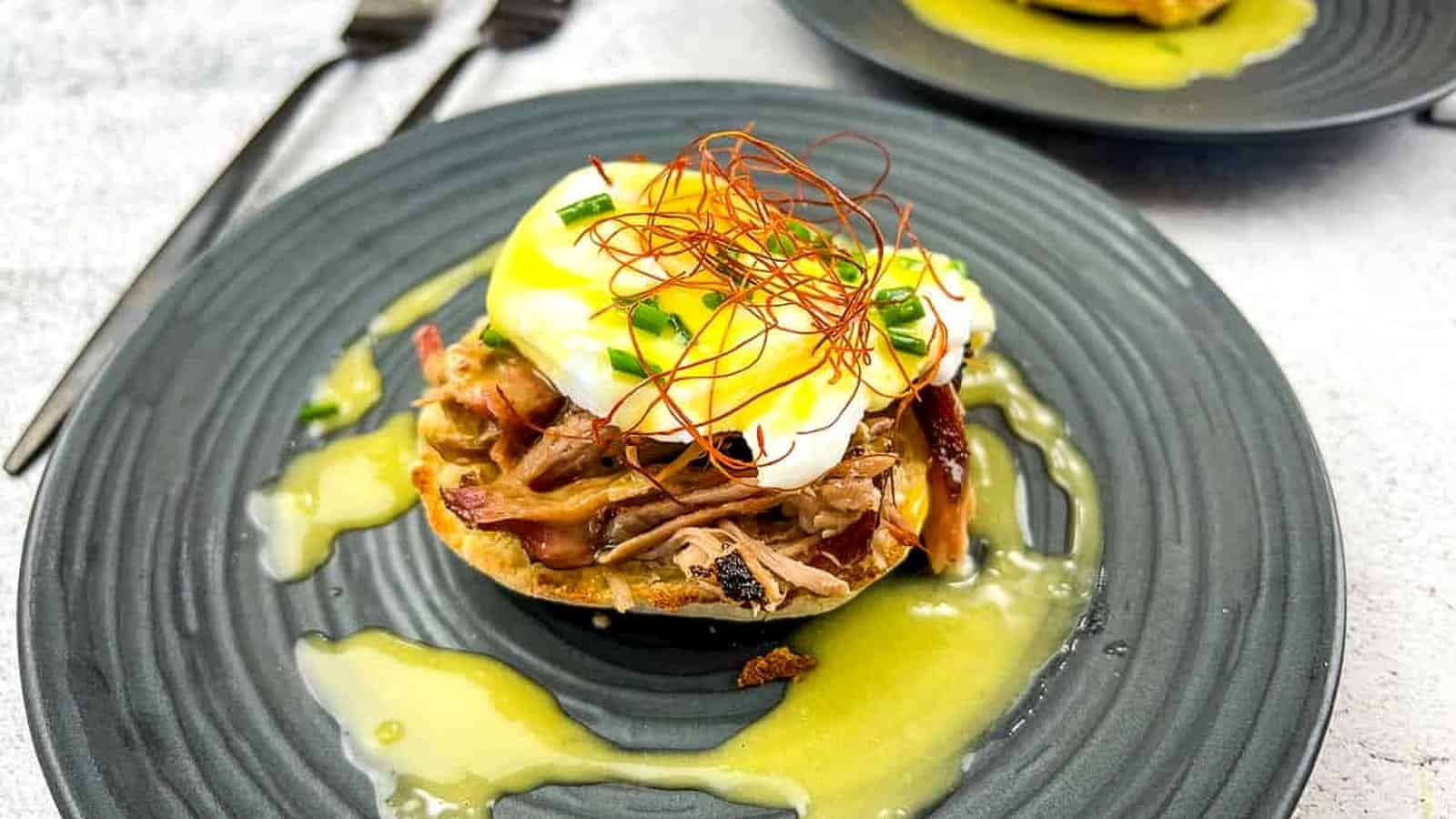 Two pulled pork eggs benedict on a plate with sauce.
