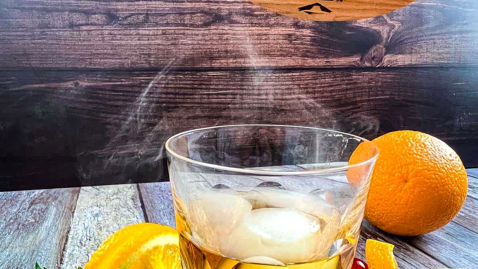 A glass of whiskey with oranges and a wooden stick.