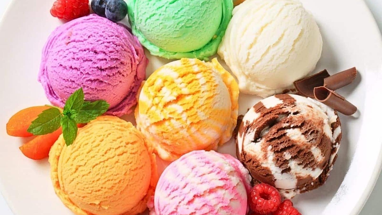 Celebrate National Ice Cream Day with six scoops of colorful ice cream, artfully arranged on a white plate and garnished with berries, two apricot slices, a mint sprig, and delicate chocolate curls.