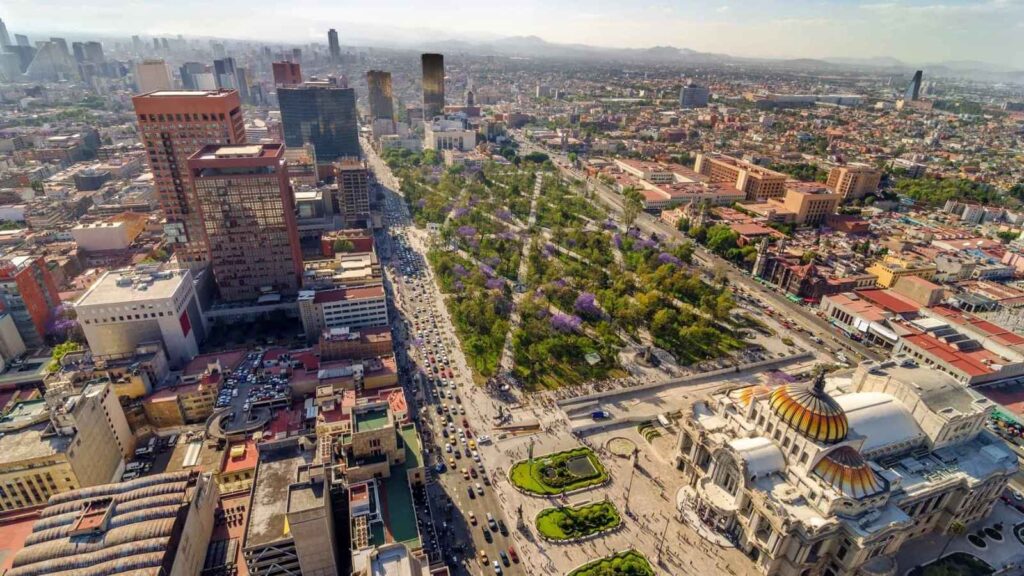 Aerial view of a busy cityscape with high-rise buildings, a major avenue, a large park with trees, and a historic domed building in the foreground.