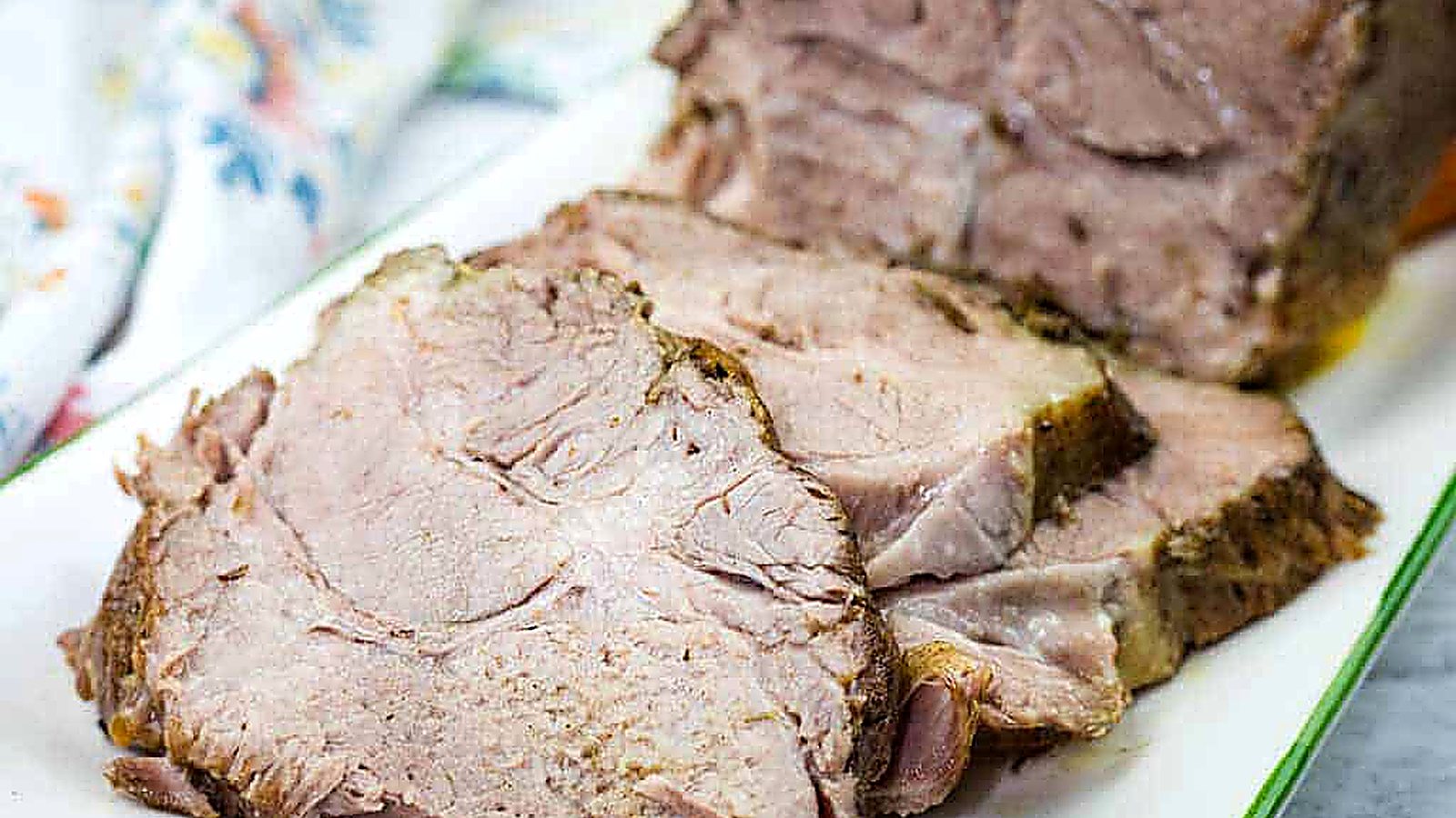 Sliced Herb-Crusted Pork Roast on a rectangular white plate with a floral napkin in the background.