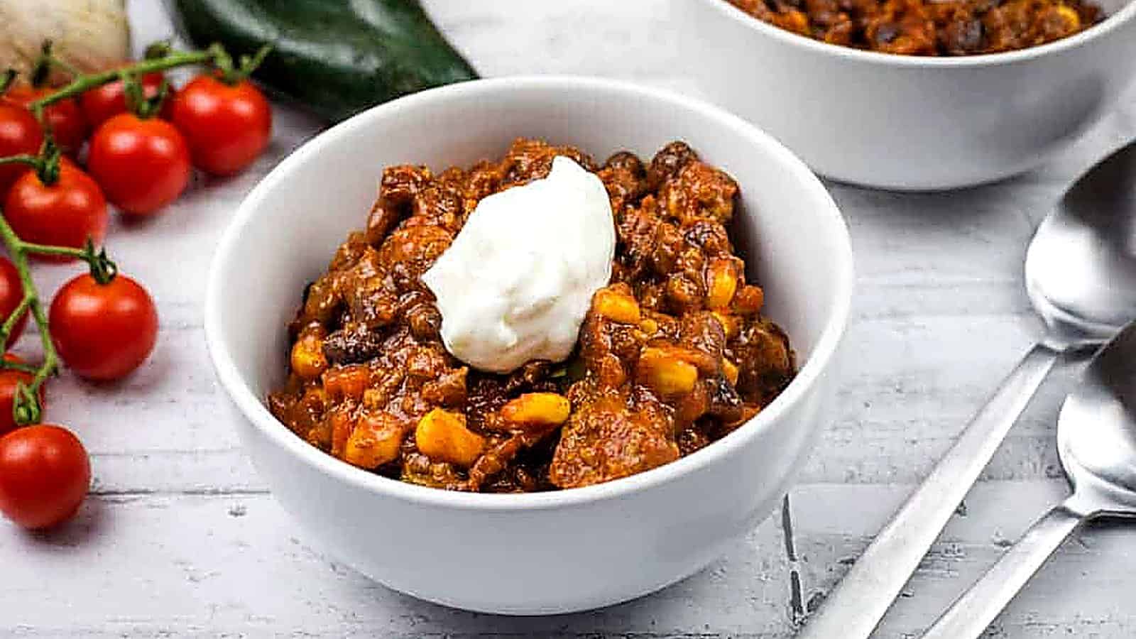 Two white bowls of Southwestern chili topped with sour cream are on a table.