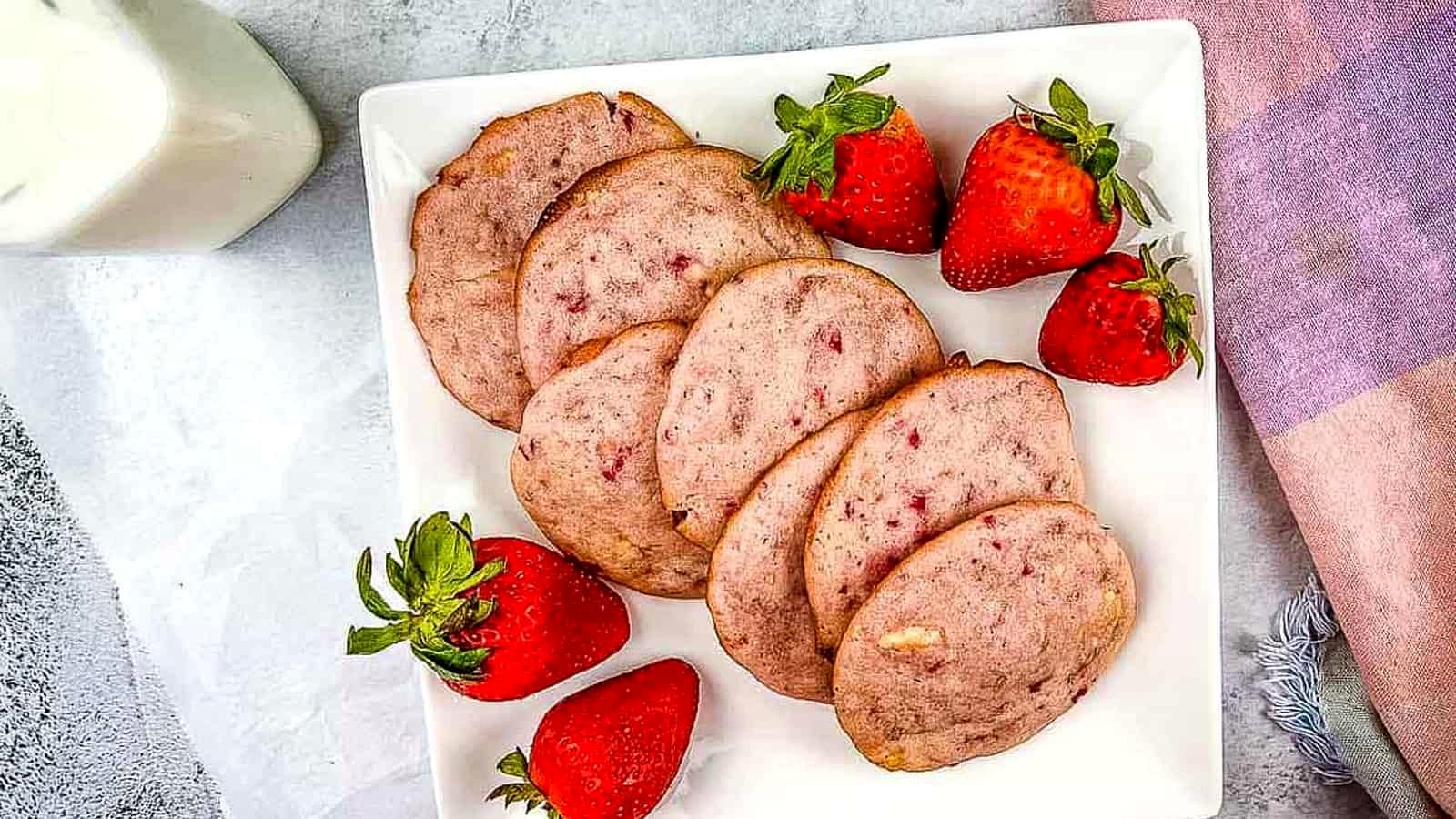 Strawberry Shortcake Cookies on a white plate with strawberries nearby.