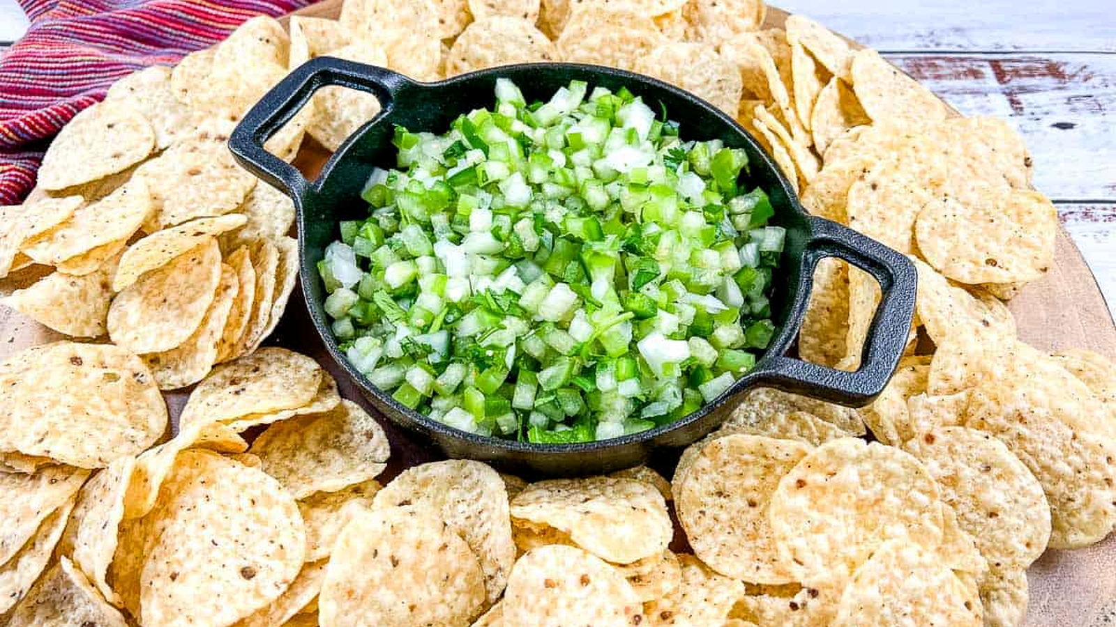Tomatillo pico de gallo in a black dish surrounded by tortilla chips.