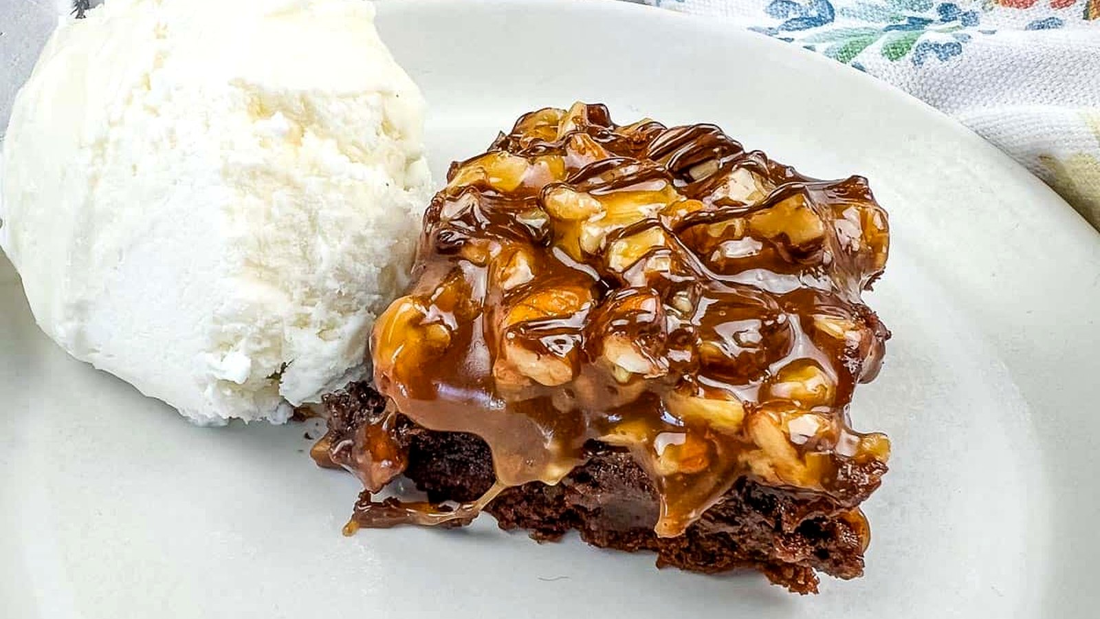 A piece of Turtle Brownie with ice cream on a plate.