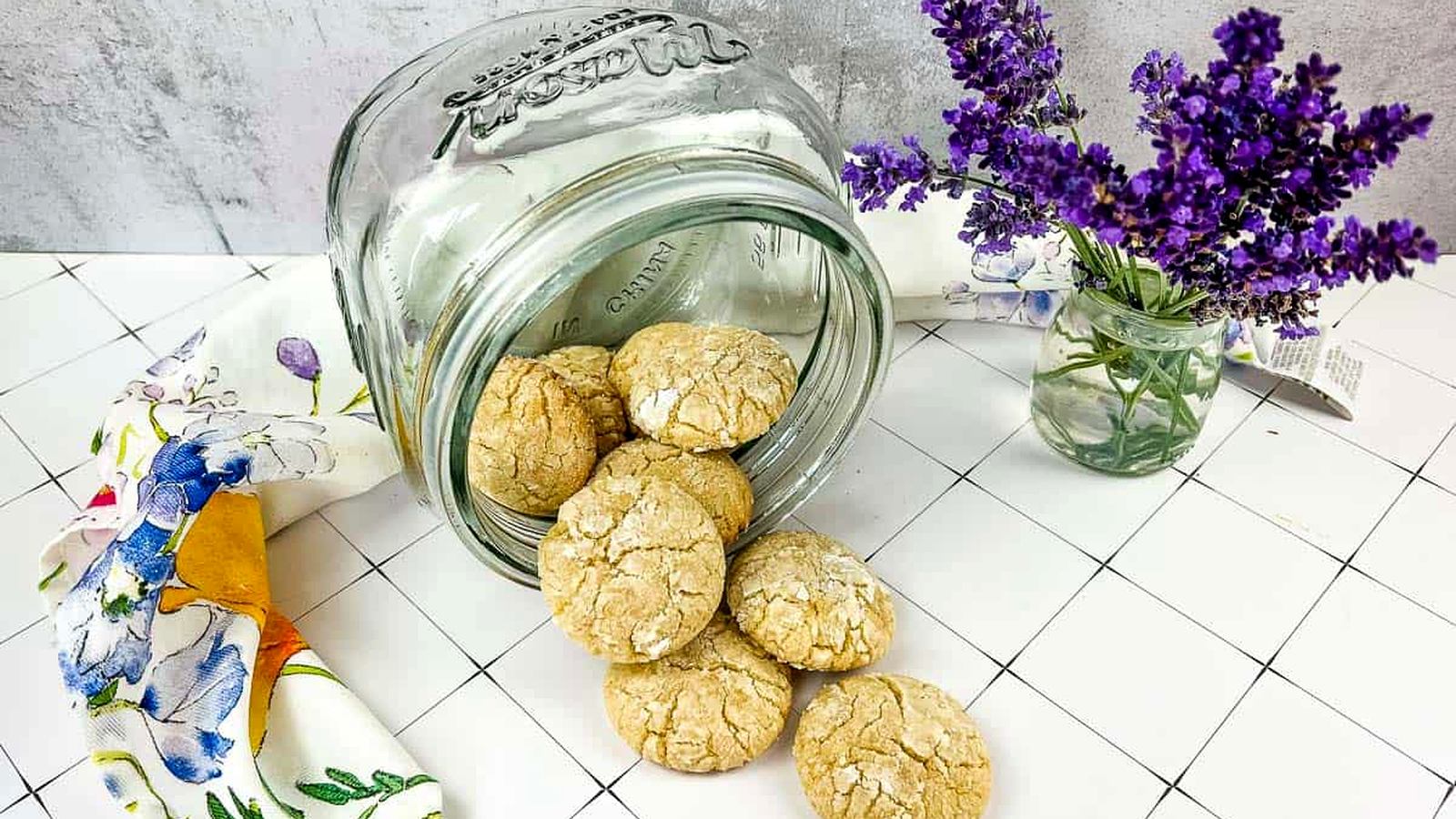 A jar of White Chocolate Crinkle Cookies next to lavender flowers.