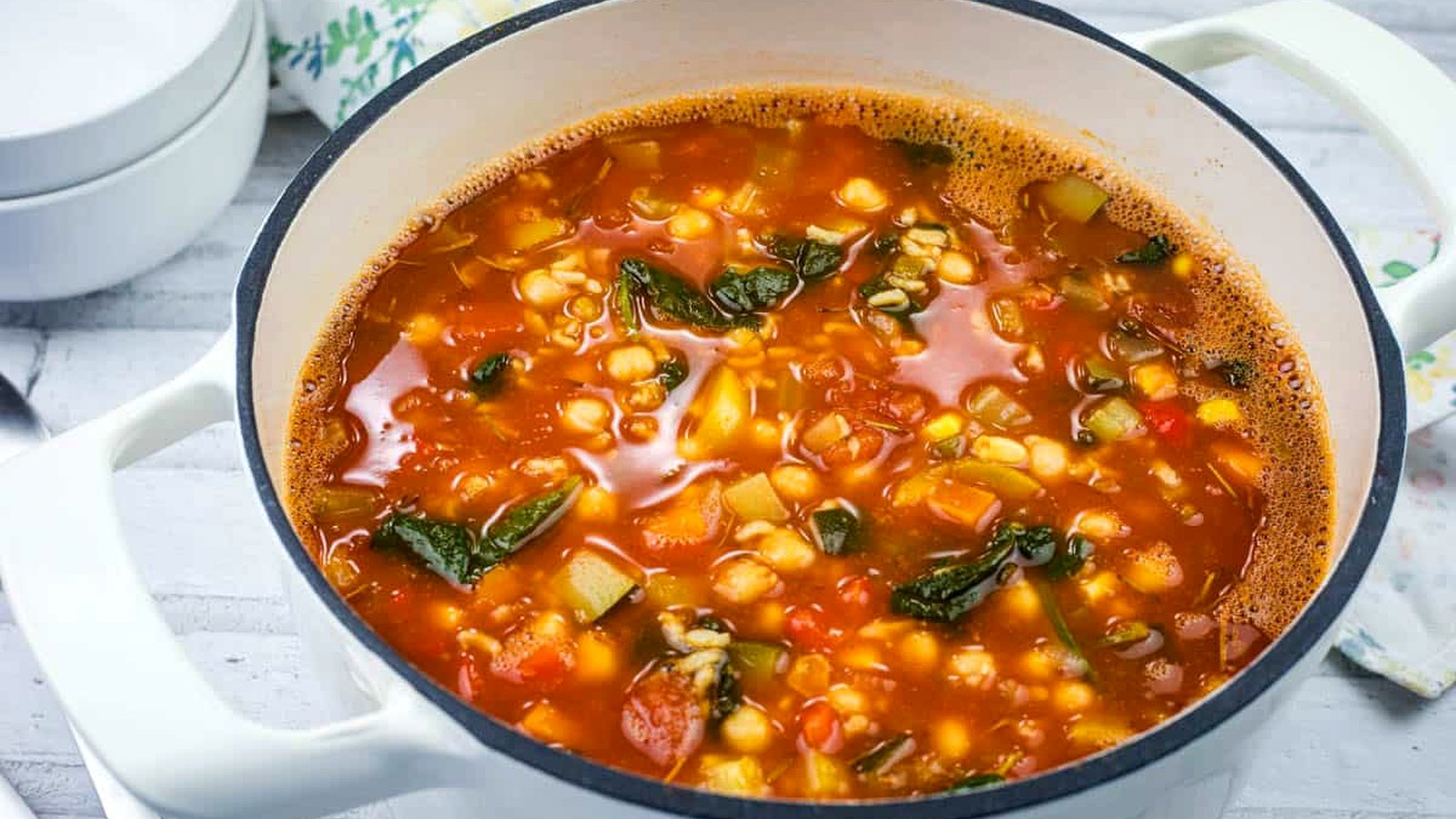 A bowl of Panera Bread’s 10 Vegetable soup with beans and greens on a white surface.