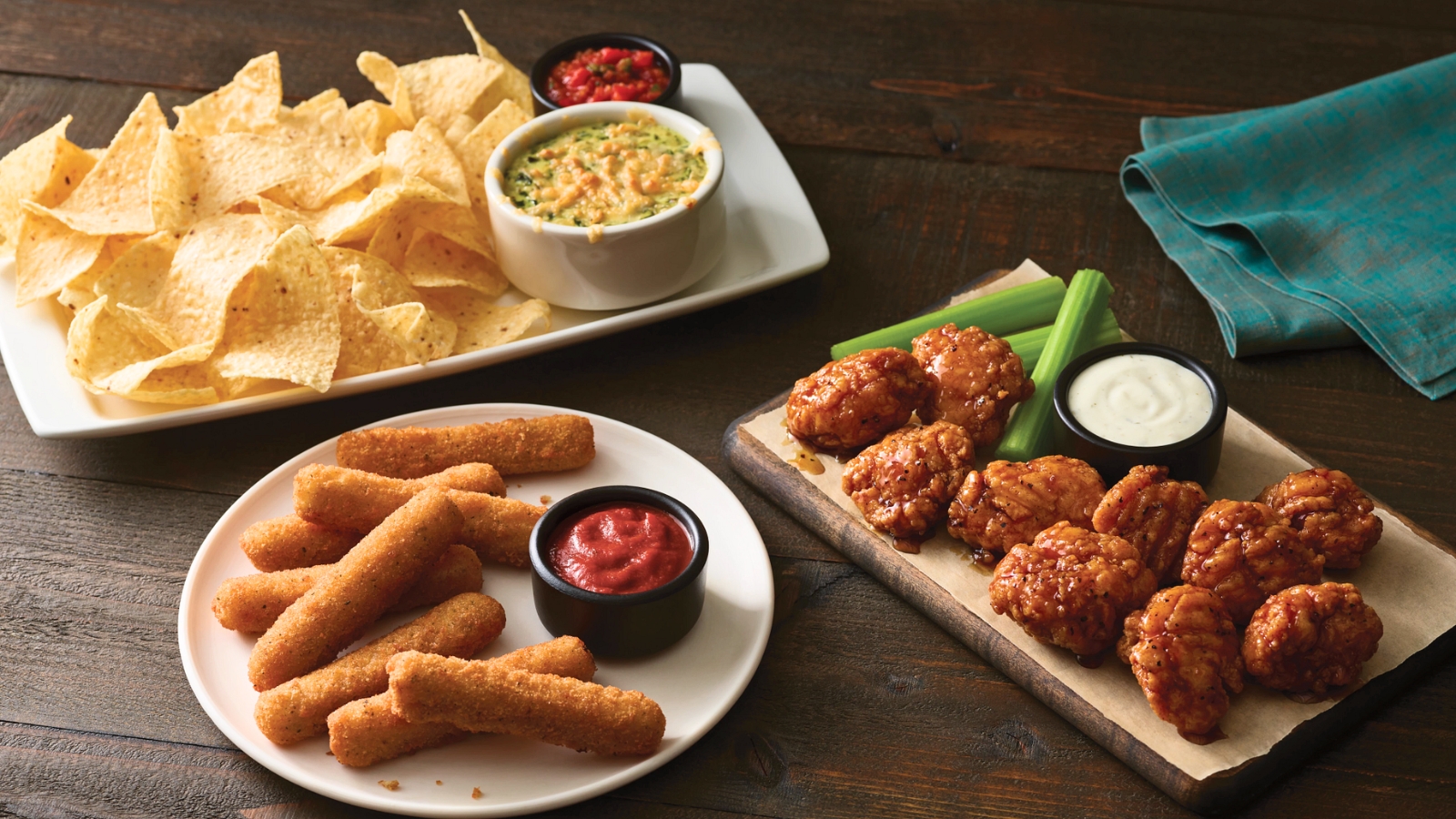 A table with tortilla chips and dip, mozzarella sticks with marinara sauce, and boneless chicken wings with celery and ranch dressing.