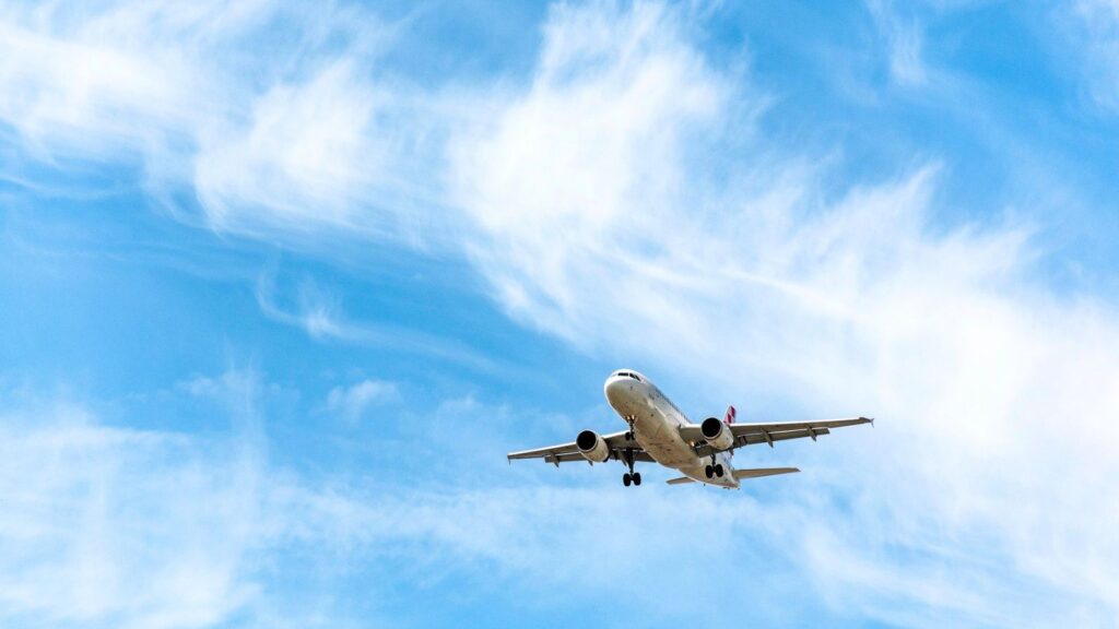 A white passenger airplane flies against a blue sky with wispy clouds, viewed from below.
