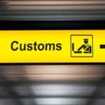 A yellow airport sign with the word “Customs,” an icon of an officer checking luggage, and a right arrow—reminding travelers to declare any items, including foods US customs will take, before proceeding.