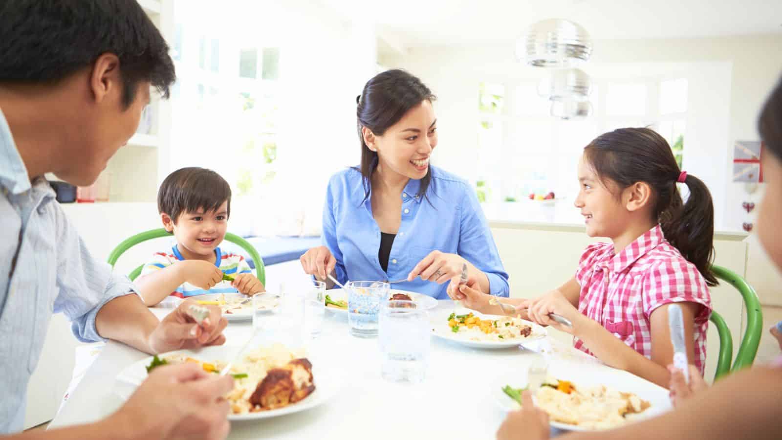 A family of four sits at a dining table eating a meal together, smiling and talking in a bright, modern kitchen, while discussing the recent changes in beef prices.