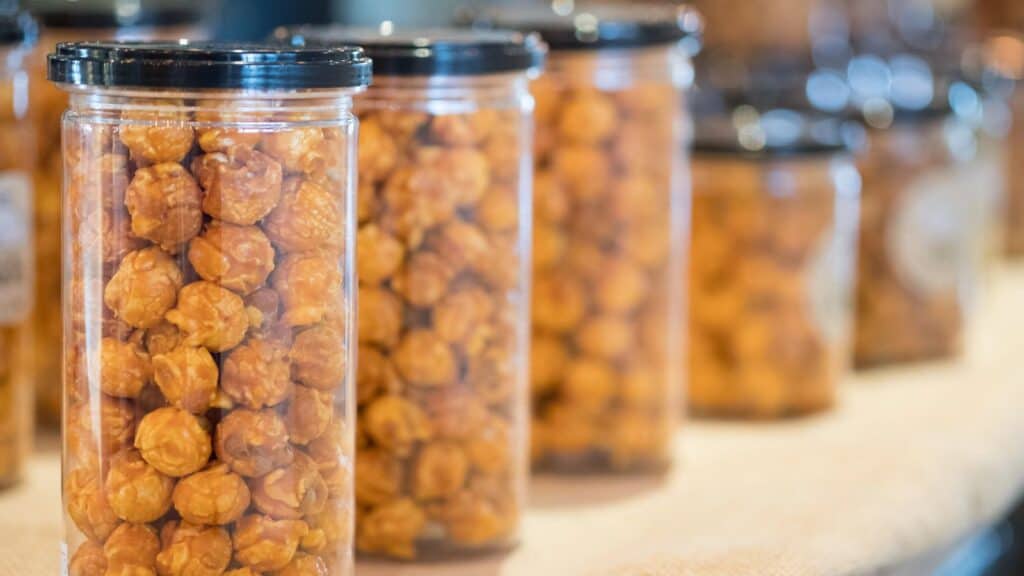 Clear plastic jars filled with caramel popcorn, a favorite among mall food court staples, are arranged in rows on a light-colored surface.
