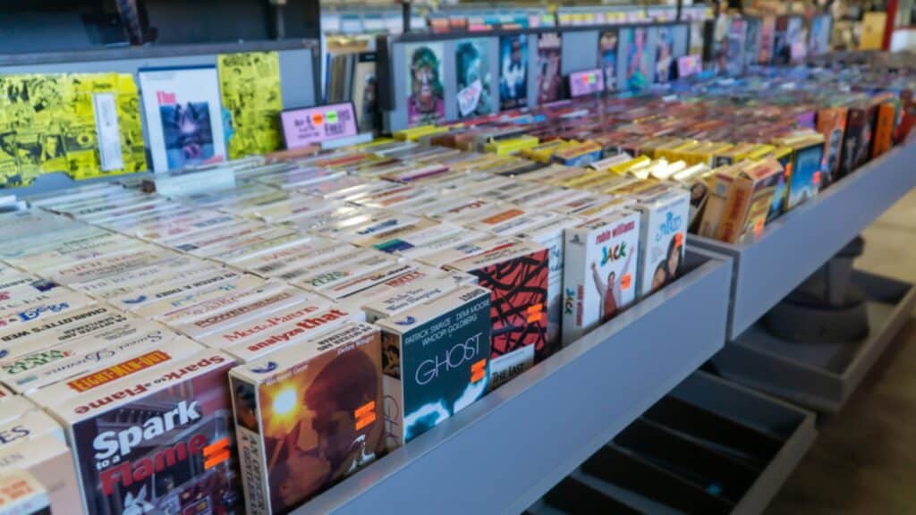 Rows of cassette tapes are displayed on shelves in a store, with colorful album covers and labels visible, creating a retro and organized appearance.