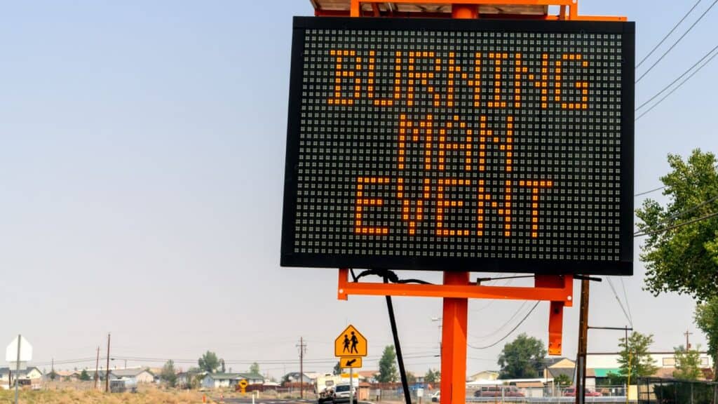 Electronic road sign displays “BURNING MAN EVENT”; residential area and school crossing sign visible in the background.