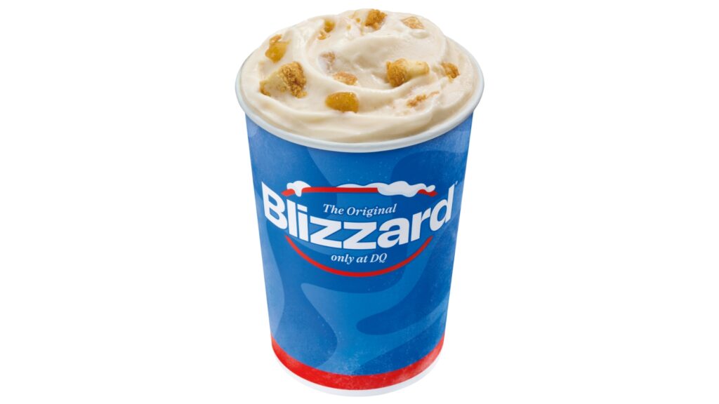 A Dairy Queen Pumpkin Pie Blizzard dessert in a blue cup, topped with chunks of cookie dough, against a white background.