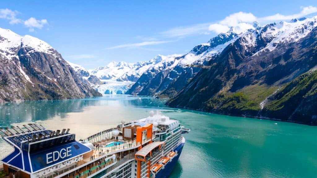 A large Celebrity Cruises ship sails through a turquoise fjord surrounded by snow-capped mountains and a glacier under a clear blue sky, showcasing the line&rsquo;s commitment to expanding to every continent.