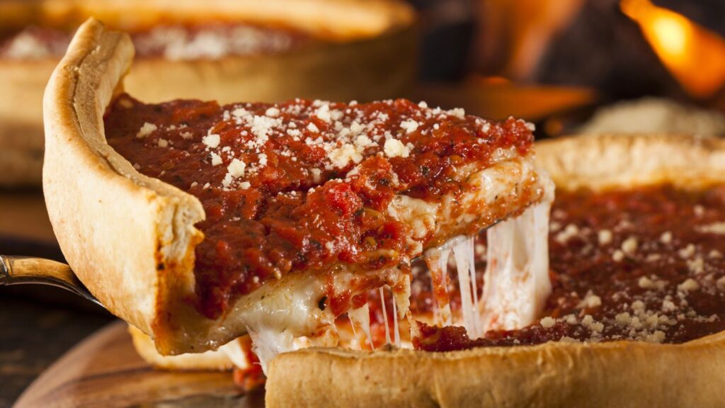 A slice of deep-dish pizza with melted cheese being lifted from a whole pizza, topped with tomato sauce and grated cheese&mdash;perfect for enjoying with your Uno Pizza Pass.