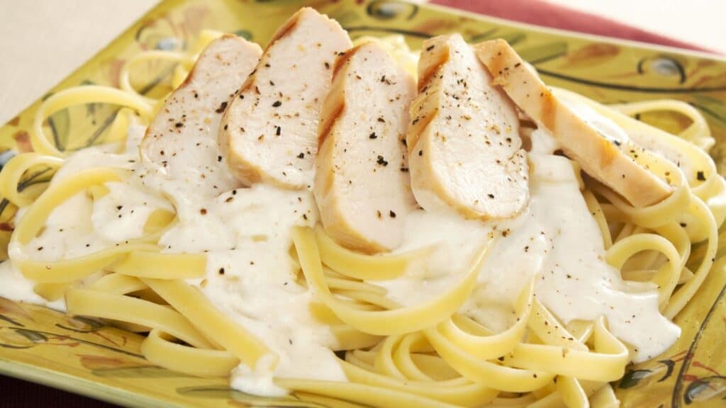 Fettuccine pasta topped with sliced grilled chicken breast and creamy white Alfredo sauce, served on a decorative square plate—crafted with the same care and quality you’d expect from top store brands companies behind the label.