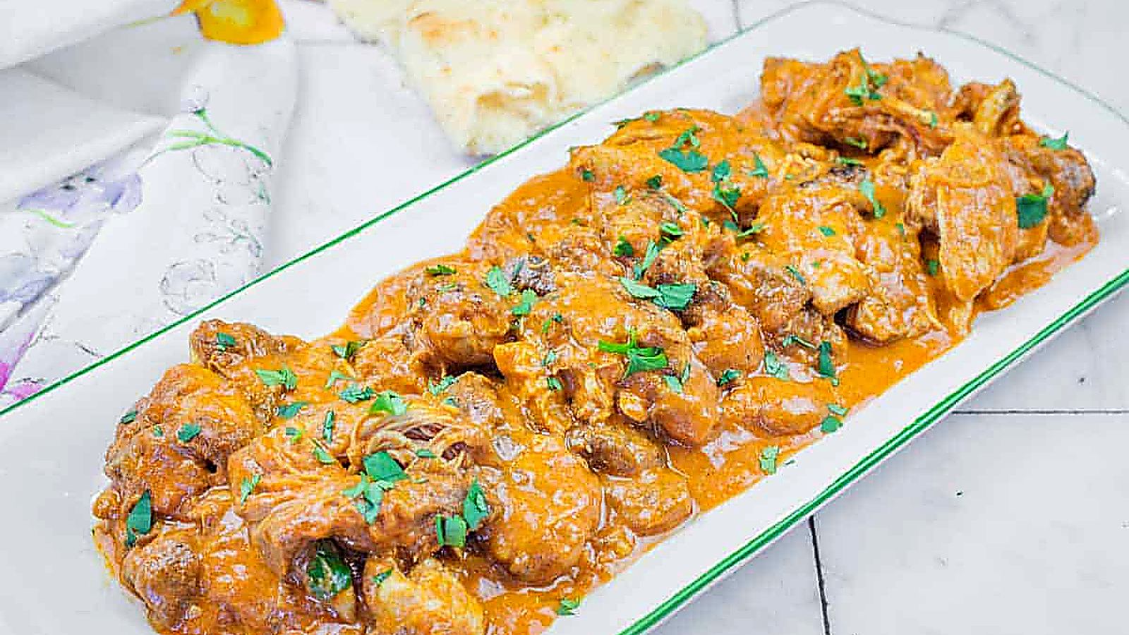 A rectangular plate of Chicken Tikka Masala with herbs on top.