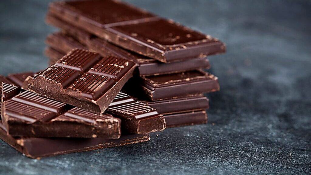 Several pieces of dark chocolate bars are stacked and scattered on a dark, textured surface.