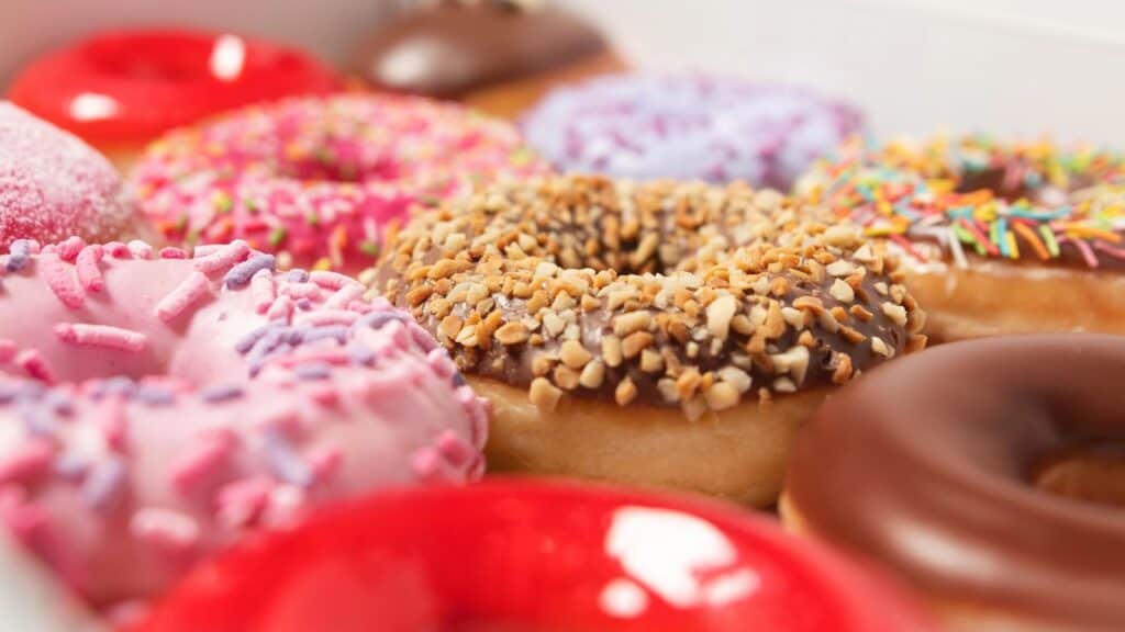 Assorted donuts with various colorful icings, sprinkles, and toppings arranged closely together&mdash;these classic American foods with foreign roots showcase a delicious blend of global inspirations in every bite.