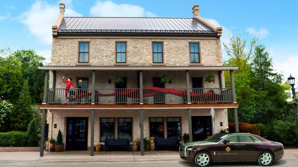 A stone two-story Kat Florence Hotel with a balcony, potted plants, and a luxury car parked in front. A person in red stands on the balcony waving.