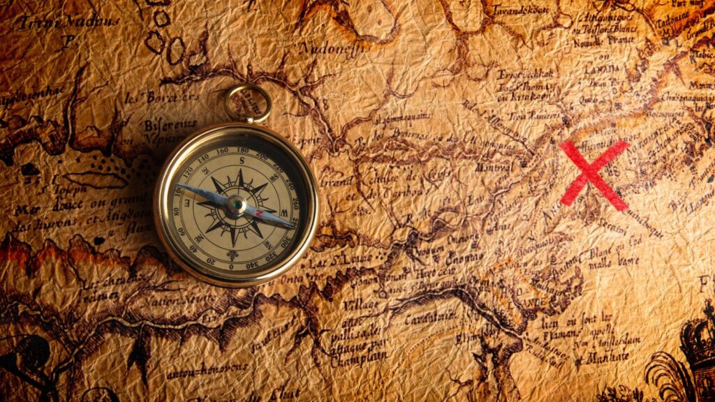 A vintage compass rests on an old, detailed treasure map with a large red X marking a location, evoking the excitement of a Grand Forks treasure hunt.