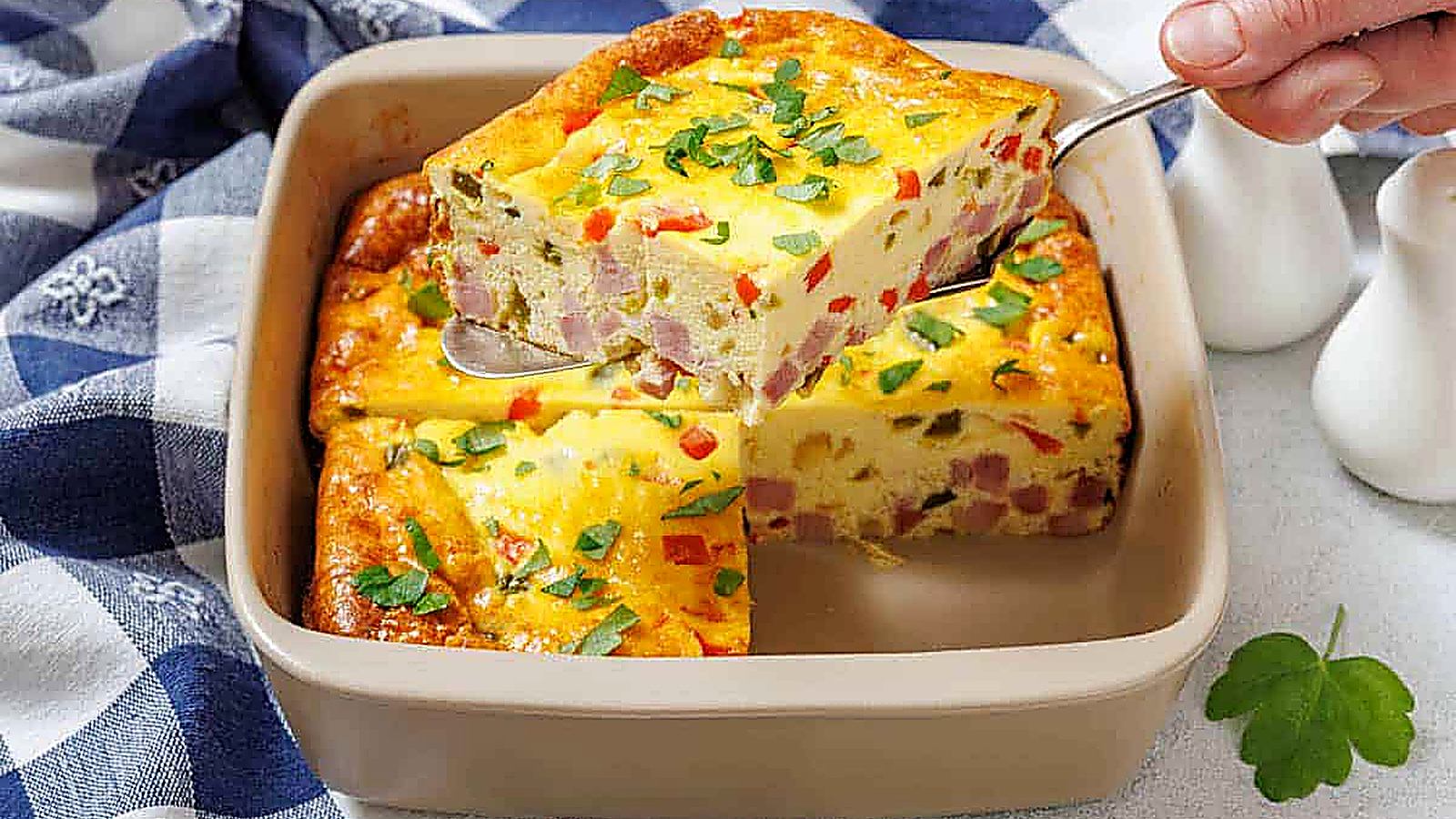 A hand holds a spatula lifting one piece of Grandma&rsquo;s Baked Western Omelet from a square dish.