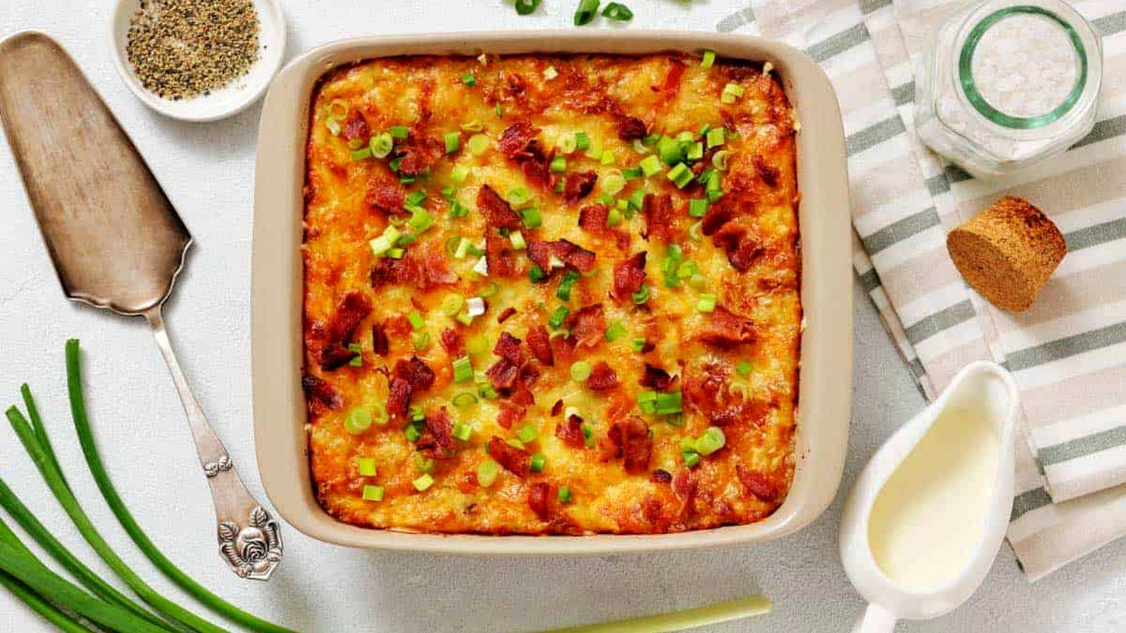 Grandma&rsquo;s Twice-Baked Potato Casserole topped with chopped green onions and bacon, surrounded by fresh green onions.