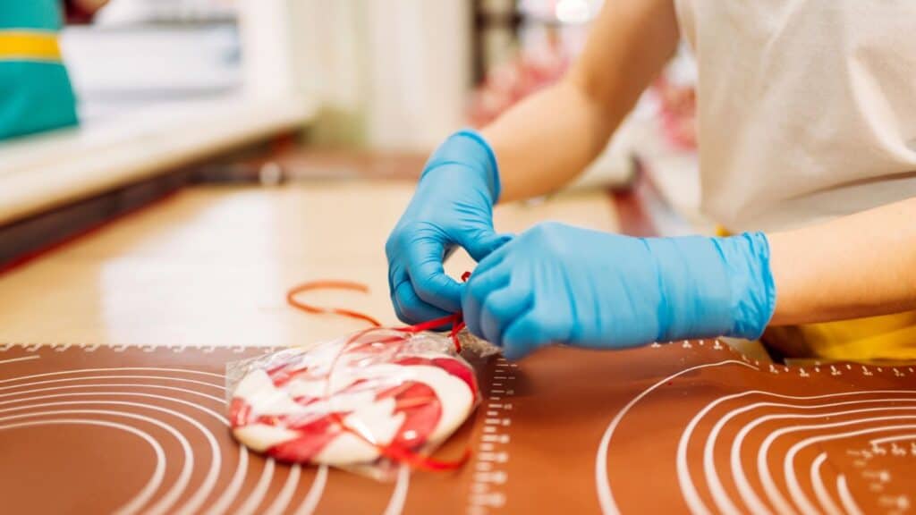 Person wearing blue gloves ties a bag containing red and white striped candy on a brown surface with circular patterns, reminding us that food labeling terms aren&rsquo;t simple.