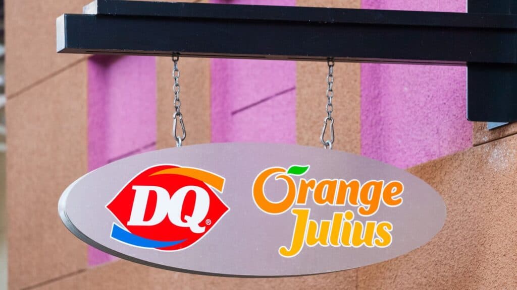 Oval sign with DQ and Orange Julius logos hangs outside a building with textured tan and purple walls, showcasing two classic mall food court staples.