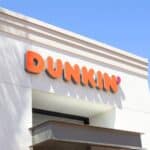 A white Dunkin’ building with an orange and pink logo on the exterior, viewed from below against a clear blue sky.