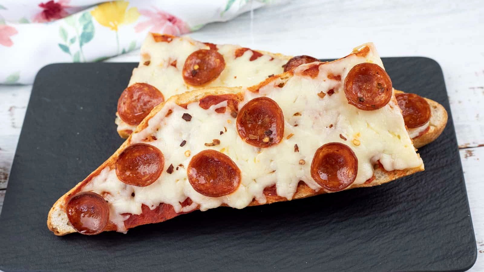Two slices of French bread pizza topped with melted cheese and pepperoni are placed on a black rectangular plate.