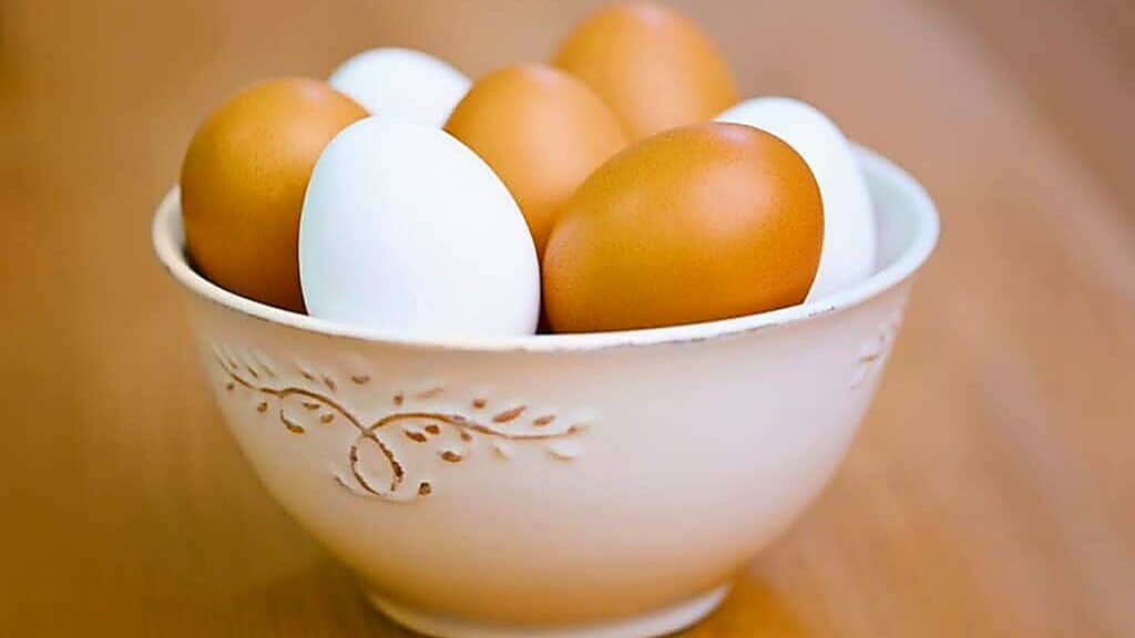 A white ceramic bowl containing brown and white eggs is placed on a wooden surface.