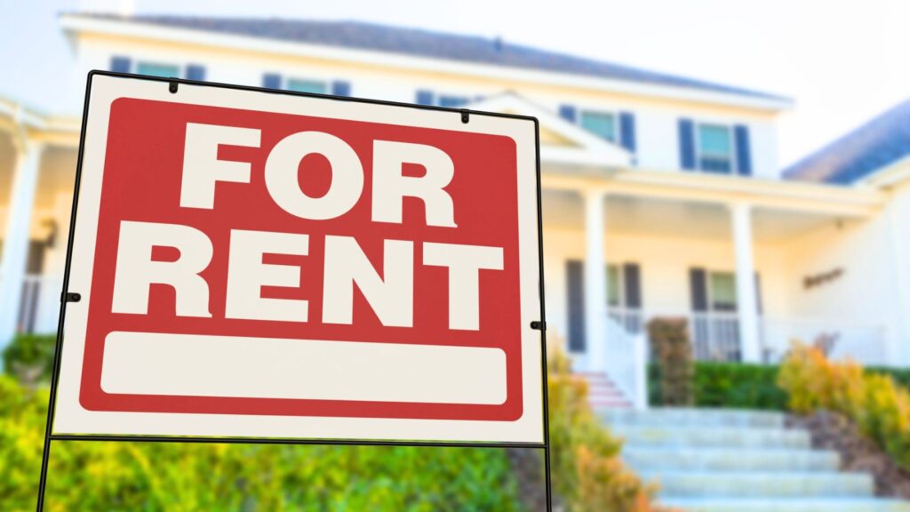 Large &ldquo;For Rent&rdquo; sign is displayed in front of a suburban house with steps and a porch, indicating that the property is available for lease.