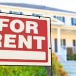 Large “For Rent” sign is displayed in front of a suburban house with steps and a porch, indicating that the property is available for lease.