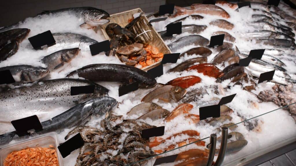 Various types of fresh fish, shrimp, crab, and lobster&mdash;grocery items whose prices rose&mdash;are displayed on ice at a seafood market counter, with blank black price tags.