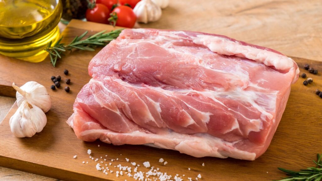 Raw pork belly on a wooden cutting board with garlic, rosemary, black pepper, cherry tomatoes, salt, and a bottle of olive oil nearby&mdash;ingredients carefully chosen as more Americans eat according to stricter EU rules for quality and food safety.