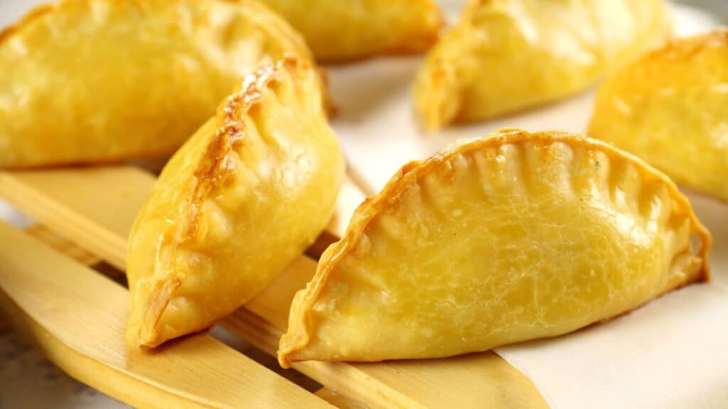 Golden-brown baked empanadas arranged on a wooden board, showing a flaky, crimped edge and glossy finish&mdash;echoing the care found in traditional foods with protected names in Europe.