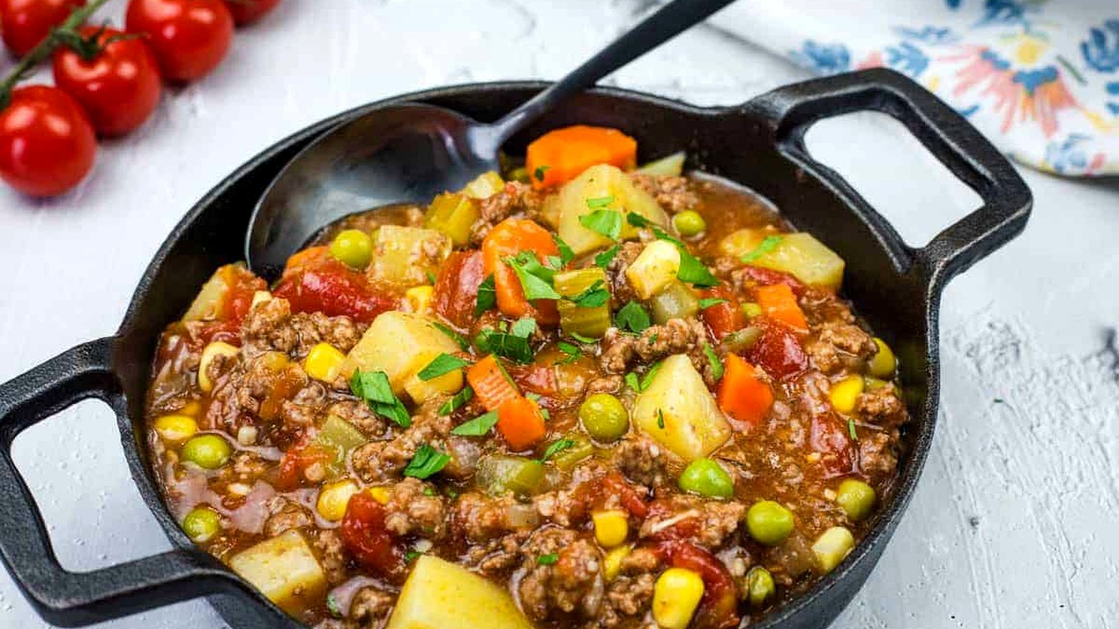 A cast iron skillet filled with Mom&rsquo;s Hamburger Stew garnished with herbs.