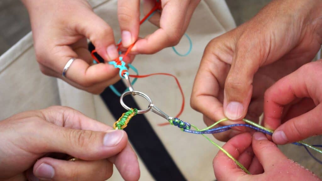 Four hands braid colorful strings onto a metal ring, working together on a craft project&mdash;a scene filled with the summer camp traditions campers remember for years to come.