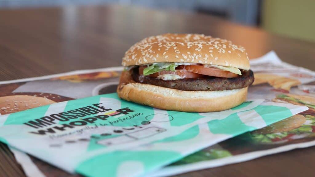 A plant-based Impossible Whopper burger, inspired by fast-food items started locally, with lettuce, tomato, and sauce sits on its branded wrapper on a table.