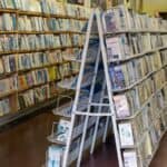 Rows of shelves filled with books and magazines are seen in a library or bookstore with a wooden counter in the background.